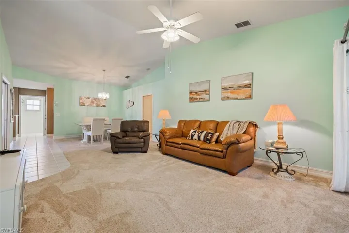 Carpeted living area with vaulted ceiling, a chandelier, ceiling fan, and tile patterned floors