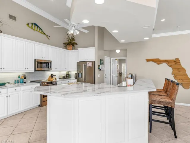 Kitchen featuring ceiling fan, stainless steel appliances, white cabinets, decorative backsplash, and a kitchen breakfast bar