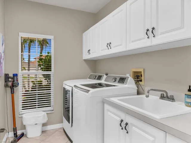 Laundry room with cabinets, separate washer and dryer, light tile patterned flooring, and sink