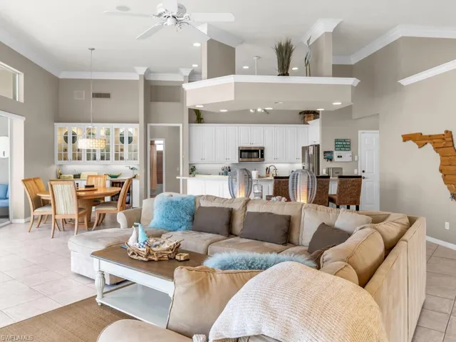 Living room with light tile patterned floors, ceiling fan, crown molding, and a high ceiling
