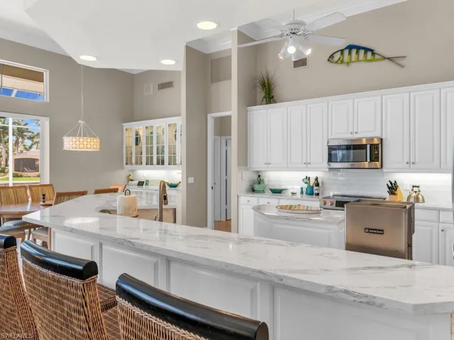 Kitchen with white cabinetry, pendant lighting, a center island, light stone countertops, and backsplash