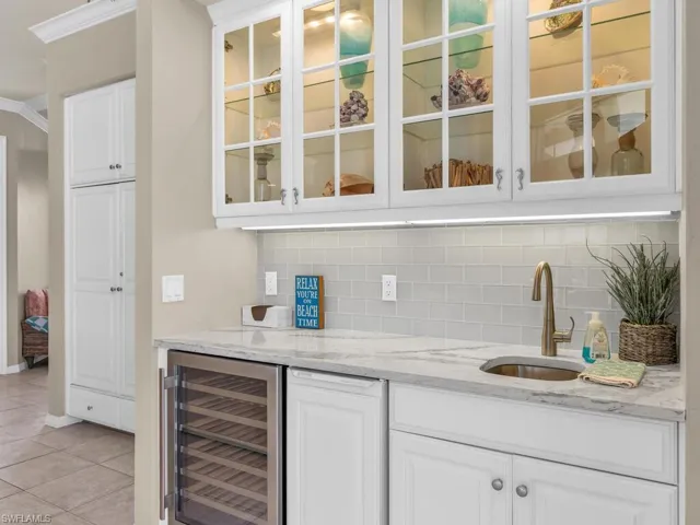 Bar with white cabinets, beverage cooler, backsplash, light stone countertops, and sink