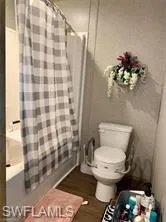 Bathroom featuring shower / bath combination with curtain, hardwood / wood-style floors, and toilet