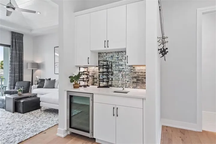 Indoor wet bar featuring white cabinetry, wine cooler, light stone counters, and light wood-type flooring