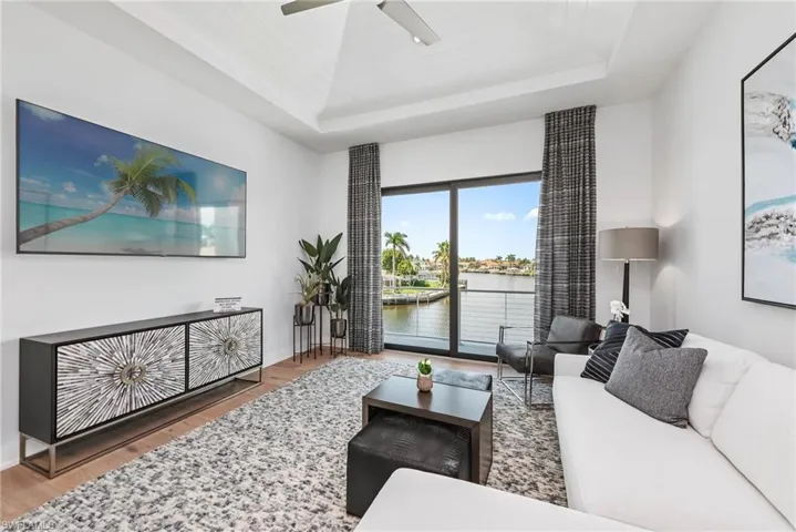 Living area featuring wood finished floors, a water view, a ceiling fan, and a tray ceiling