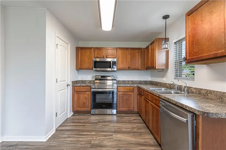 Kitchen with dark countertops, stainless steel appliances, dark wood-style floors, brown cabinetry, and hanging light fixtures