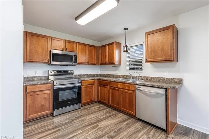 Kitchen featuring stainless steel appliances, dark countertops, brown cabinets, wood finished floors, and hanging light fixtures
