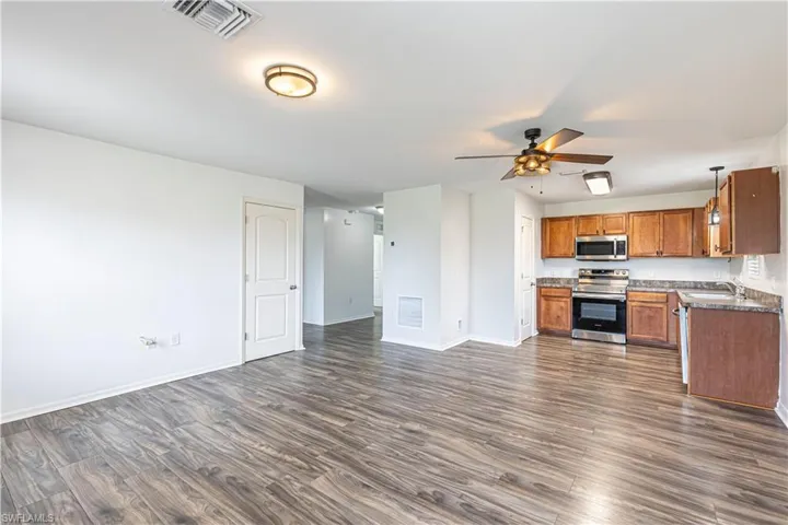 Kitchen with open floor plan, stainless steel appliances, dark wood-type flooring, and brown cabinets