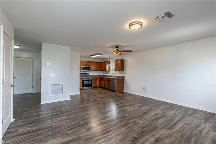 Kitchen featuring open floor plan, dark wood-style floors, appliances with stainless steel finishes, and ceiling fan