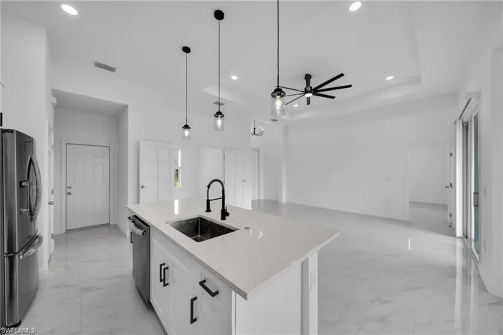 Open-concept living area featuring a kitchen island with sink, white shaker cabinetry with black hardware, recessed lighting, and a ceiling fan