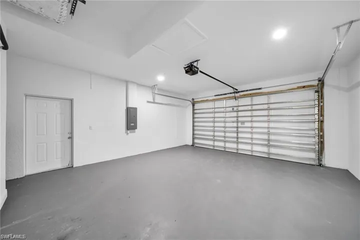 Spacious garage featuring a painted concrete floor, white walls, and a large overhead garage door with opener