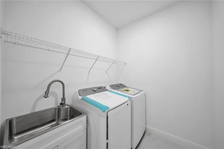Laundry area featuring a utility sink, mounted wire shelving, and light-toned flooring