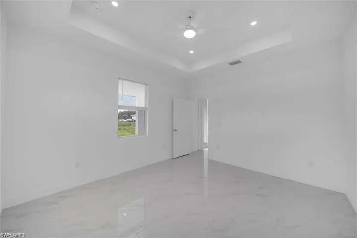 Spacious room featuring light-toned walls, large format tile flooring, a tray ceiling with recessed lighting, and a ceiling fan