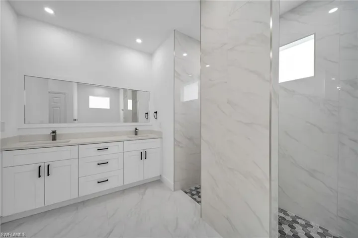 Bathroom featuring a dual vanity with white cabinetry and dark hardware, light-colored countertops, and a full-width mirror