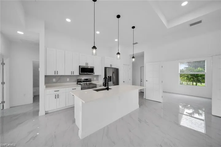 Modern kitchen featuring white shaker cabinetry, stainless steel appliances, a white quartz island with a black faucet, pendant lighting, and large format polished tile flooring