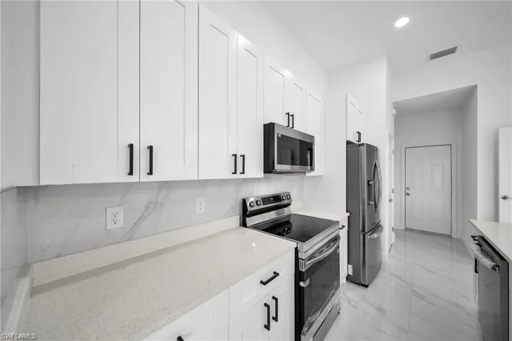 Modern kitchen featuring white shaker cabinetry, light-toned countertops, a full height backsplash with subtle veining, and a stainless steel appliance suite