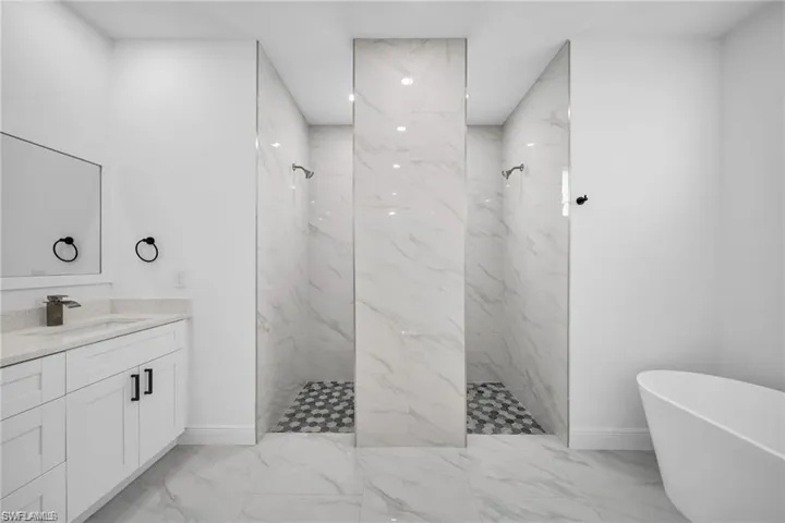 Contemporary bathroom featuring a freestanding tub, a vanity with stone-look countertop, and a double walk-in shower with large format tile walls and hexagonal floor tiles