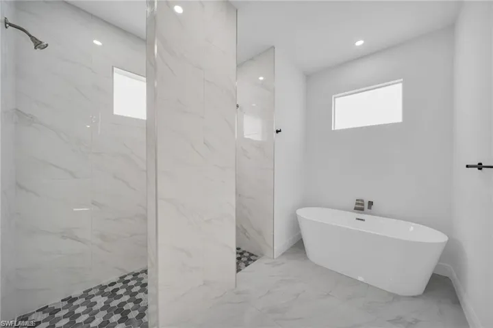 Contemporary bathroom featuring a freestanding soaking tub, two walk-in showers with hexagonal tile flooring, large format tile walls, and recessed lighting