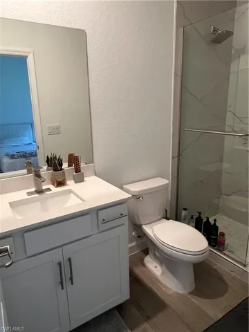 Ensuite bathroom featuring a textured wall, dark wood-style floors, vanity, and a marble finish shower