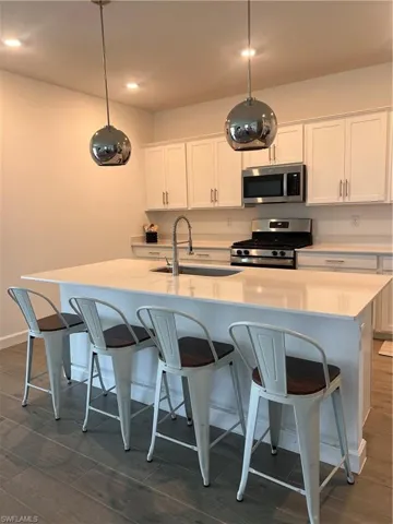 Kitchen with white cabinetry, dark wood-style flooring, stove, a kitchen breakfast bar, and white microwave