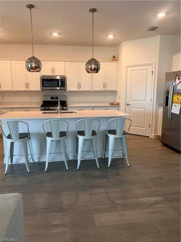 Kitchen with white cabinets, refrigerator, an island with sink, a kitchen bar, and pendant lighting