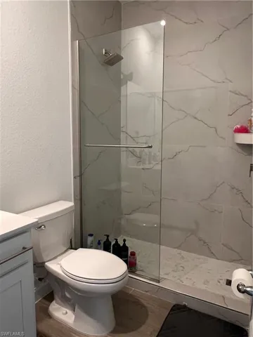 Bathroom with a marble finish shower, a textured wall, vanity, and wood finished floors