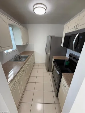 Kitchen with range with electric stovetop, light tile patterned flooring, white cabinets, and dark stone countertops