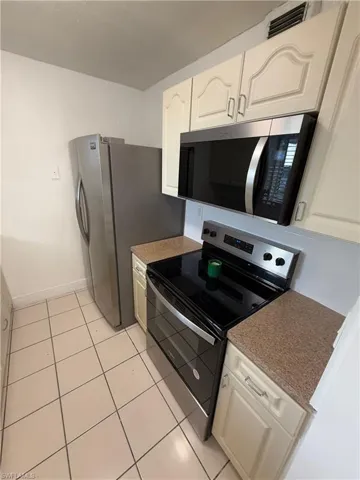 Kitchen featuring appliances with stainless steel finishes, white cabinetry, and light tile patterned floors