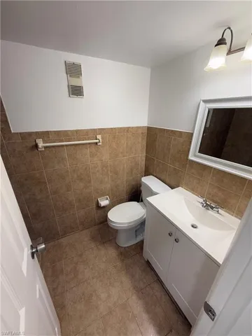 Half bath featuring vanity, tile walls, light tile patterned floors, and wainscoting