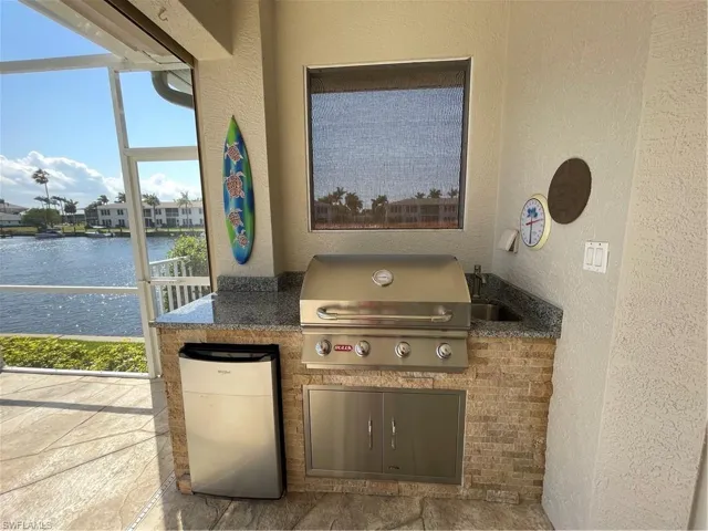 View of patio / terrace featuring an outdoor kitchen, area for grilling, a sink, a water view, and a lanai