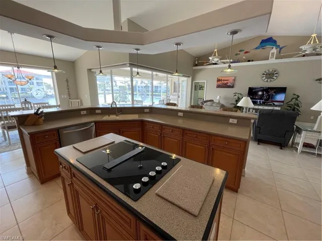 Kitchen with stovetop, a kitchen island with sink, vaulted ceiling, dishwasher, and brown cabinets
