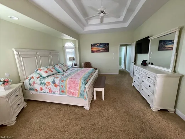 Carpeted bedroom featuring a tray ceiling, baseboards, and a ceiling fan