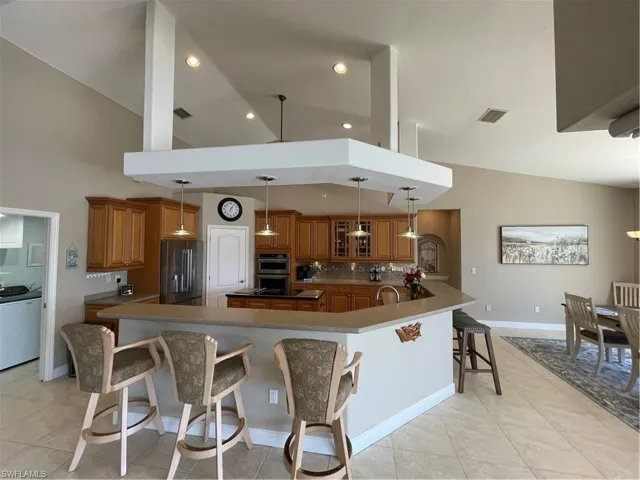 Kitchen with fridge, visible vents, a breakfast bar area, and brown cabinetry