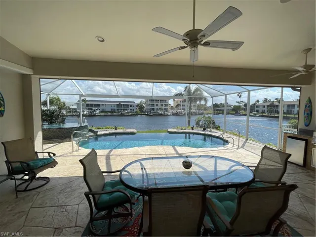 Pool featuring glass enclosure, a hot tub, ceiling fan, a water view, and a patio area