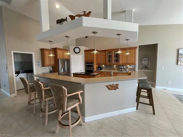 Kitchen featuring fridge, double oven, a breakfast bar area, brown cabinetry, and decorative backsplash