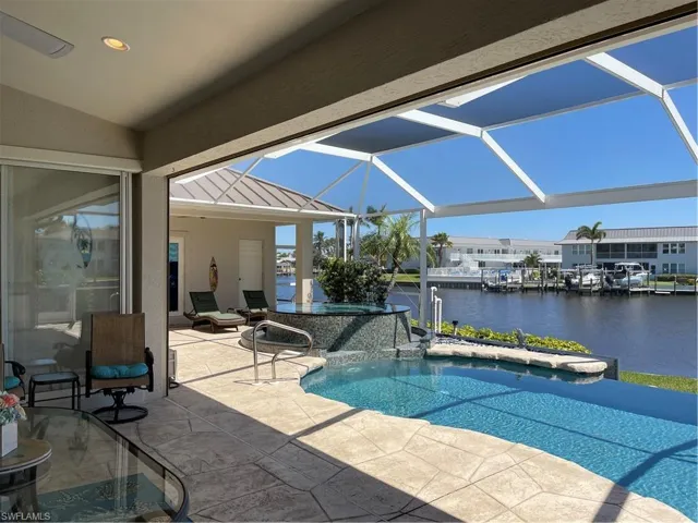 Outdoor pool featuring glass enclosure, a patio, an in ground hot tub, and a water view