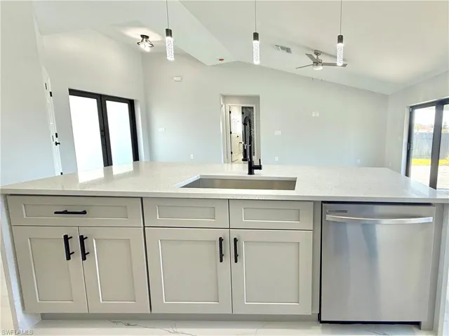 Kitchen with light stone countertops, stainless steel dishwasher, lofted ceiling, ceiling fan, and a center island with sink