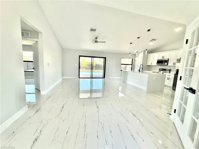 Unfurnished living room featuring vaulted ceiling, ceiling fan, light marble finish floors, and french doors