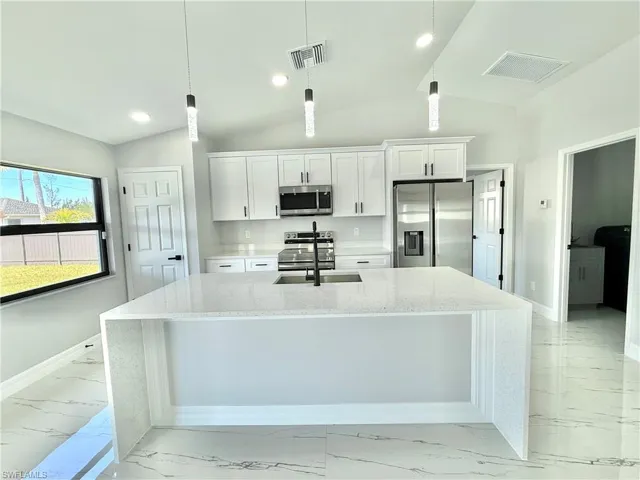 Kitchen featuring light stone counters, stainless steel appliances, light marble finish floors, white cabinets, and an island with sink