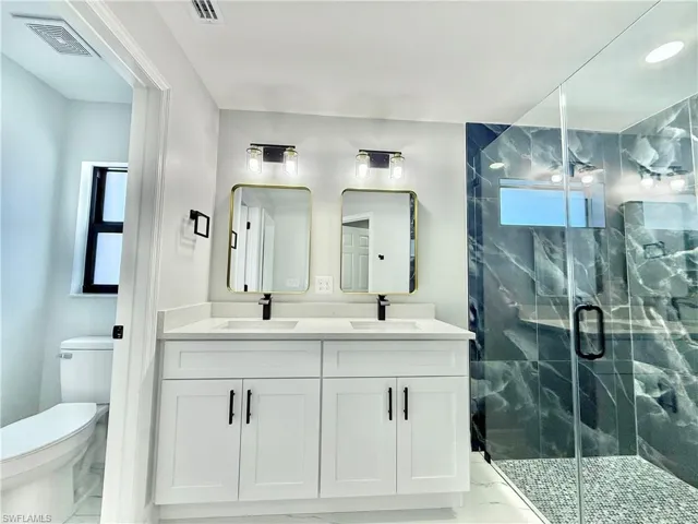 Full bathroom featuring double vanity, a marble finish shower, and light marble finish floors
