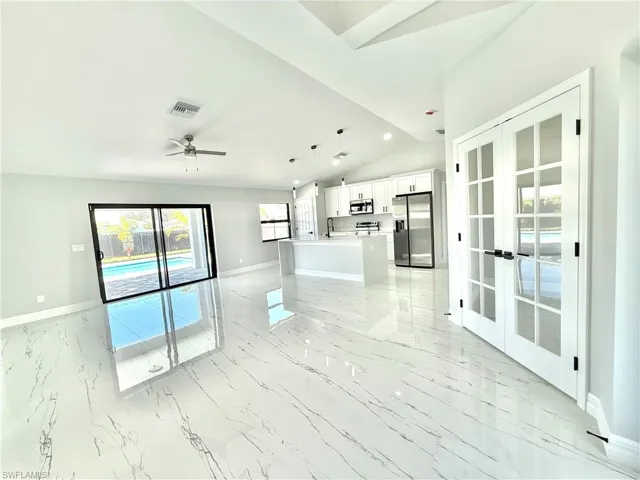 Unfurnished living room featuring a ceiling fan, light marble finish flooring, lofted ceiling, and french doors