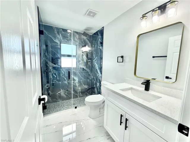 Full bath featuring vanity, a marble finish shower, and light marble finish floors