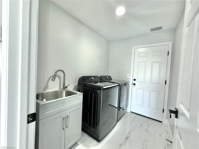 Laundry room featuring light marble finish floors, washer and dryer, and cabinet space