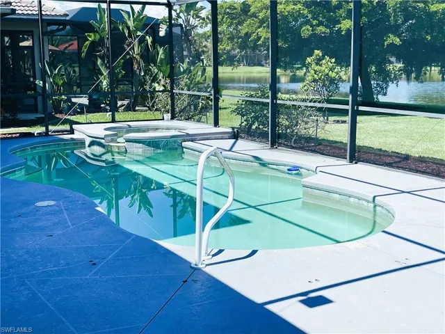 View of swimming pool with glass enclosure, a water view, and an in ground hot tub