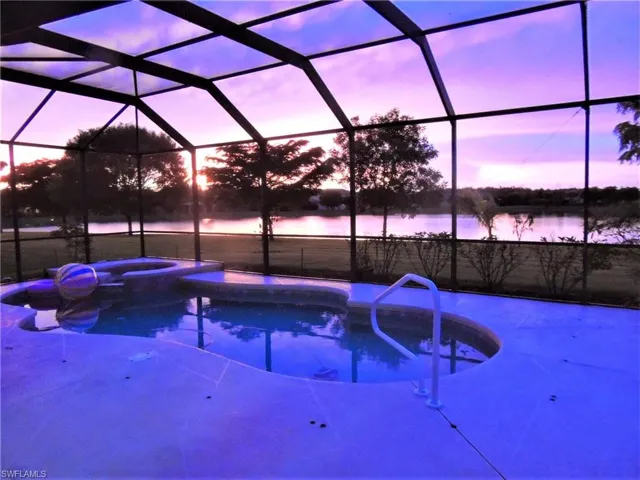 Pool at dusk featuring a water view, an in ground hot tub, and a lanai