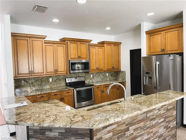 Kitchen featuring appliances with stainless steel finishes, backsplash, a textured ceiling, and light stone countertops