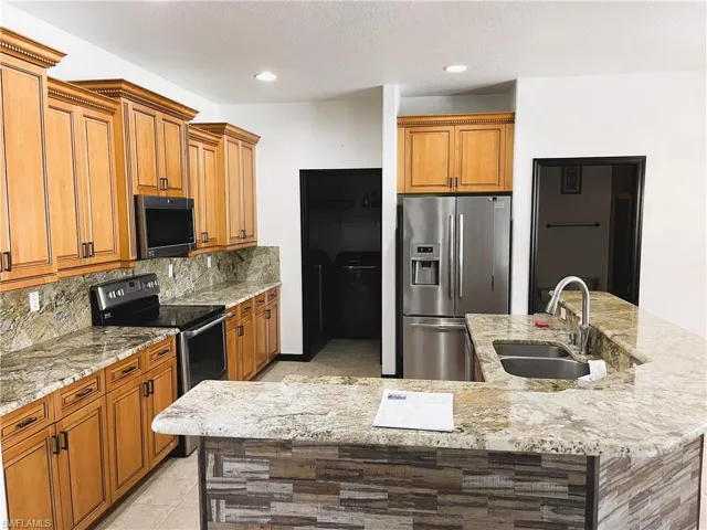 Kitchen featuring sink, a kitchen island with sink, appliances with stainless steel finishes, light stone countertops, and decorative backsplash