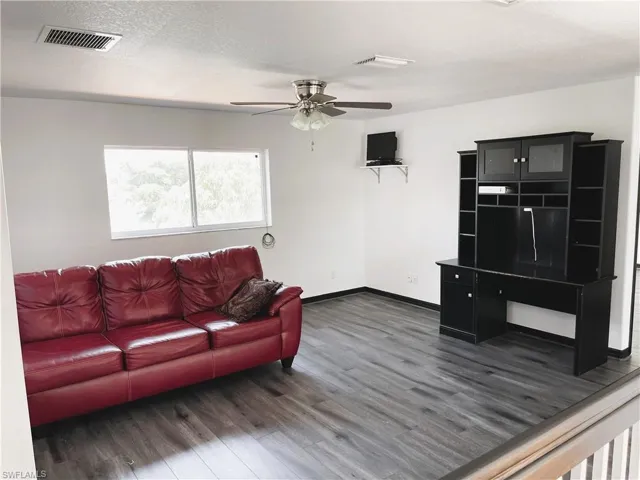 Living room with ceiling fan, a textured ceiling, and dark hardwood / wood-style floors