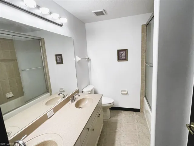 Full bathroom with bath / shower combo with glass door, vanity, toilet, and tile patterned floors