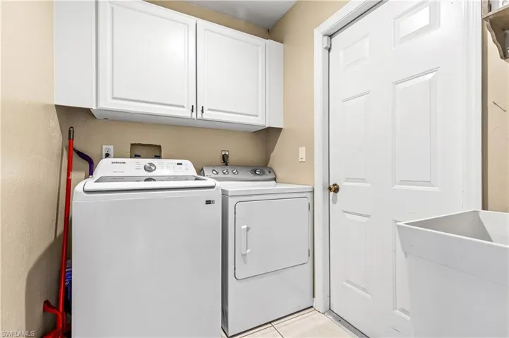 Laundry area featuring washer and clothes dryer, cabinet space, and light tile patterned flooring